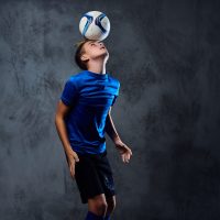 teenager soccer player dressed in a blue uniform plays with a ba
